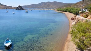 A coastal scene with boats on clear blue water, a sandy beach, and a mountainous backdrop.