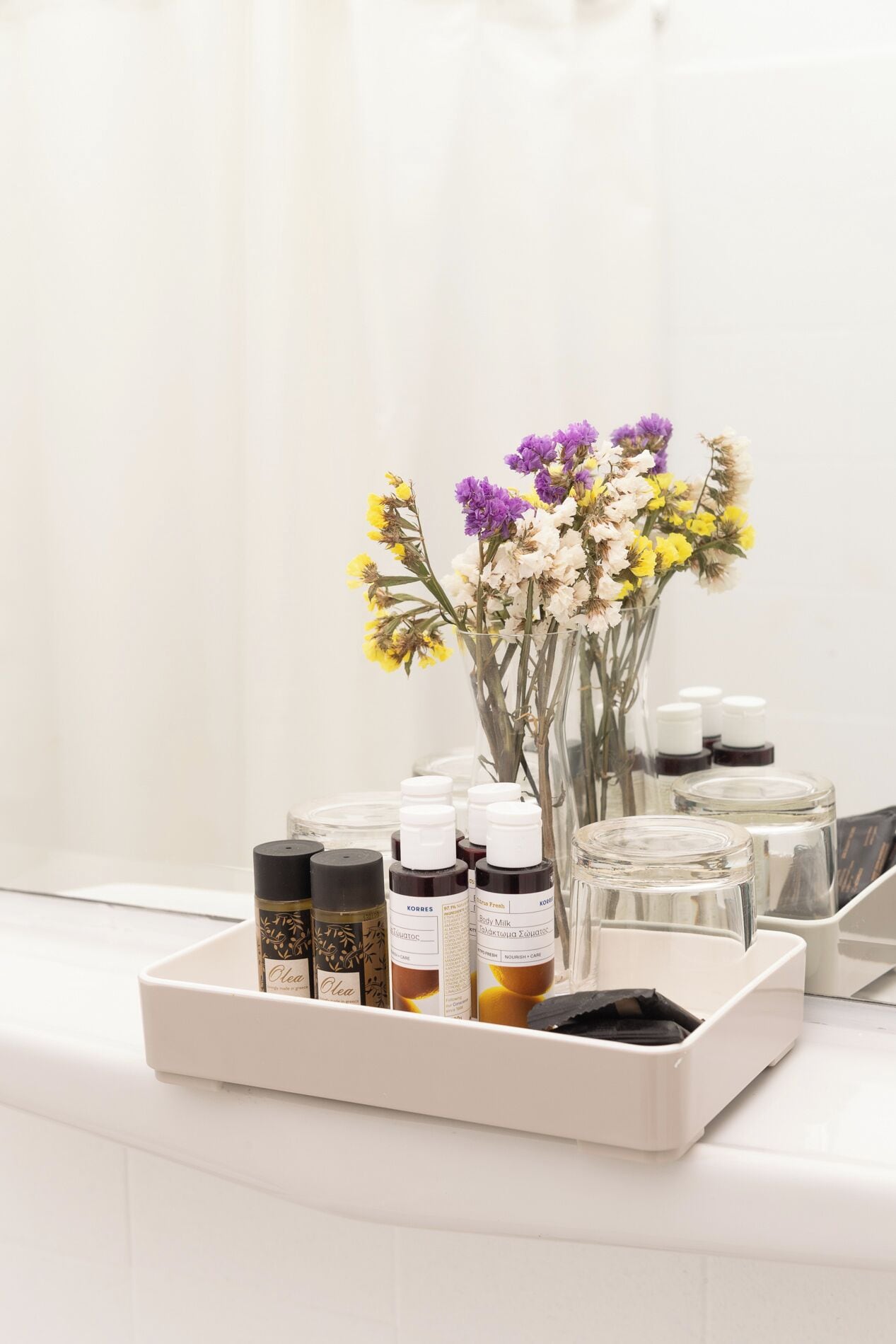 A tray with essential oils and a vase of flowers on a white countertop.