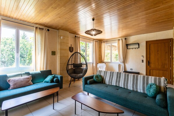 Un salon chaleureux avec deux canapés, un plafond en bois et de grandes fenêtres.