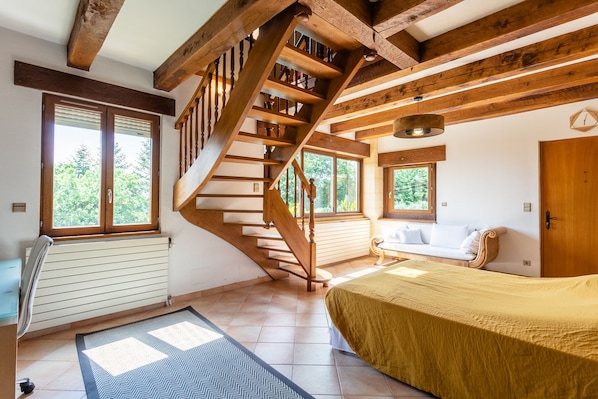 A bedroom with a wooden staircase, a bed, a sofa, and large windows.
