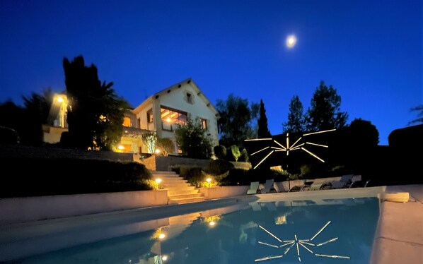 A house with a swimming pool, stairs leading up to the house, and a moon in the sky.