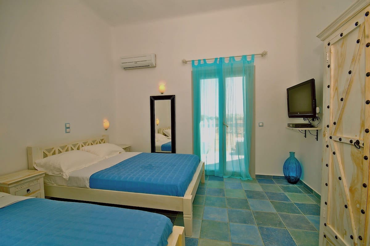 A bedroom with two beds, a TV, a mirror, and a window with curtains.