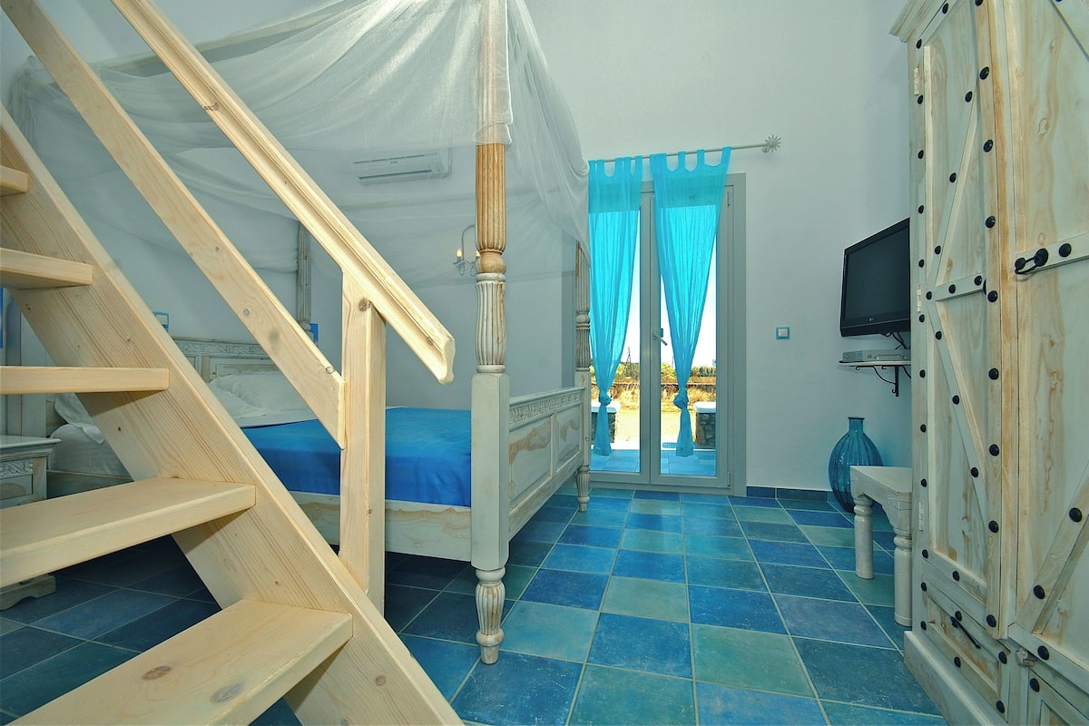 A bedroom with a bed, a wooden staircase, a TV, and a wardrobe.