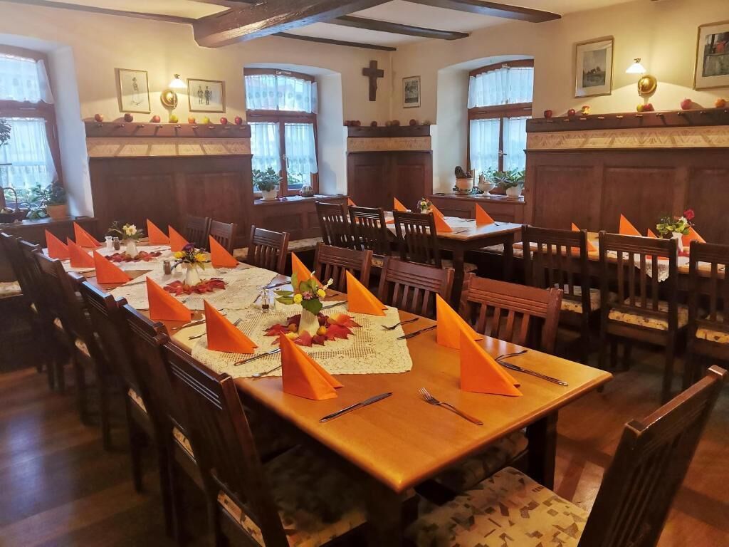 Een eetgedeelte met houten tafels en stoelen, versierd met oranje servetten en bloemige decoraties.