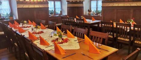 Een eetgedeelte met houten tafels en stoelen, versierd met oranje servetten en bloemige decoraties.