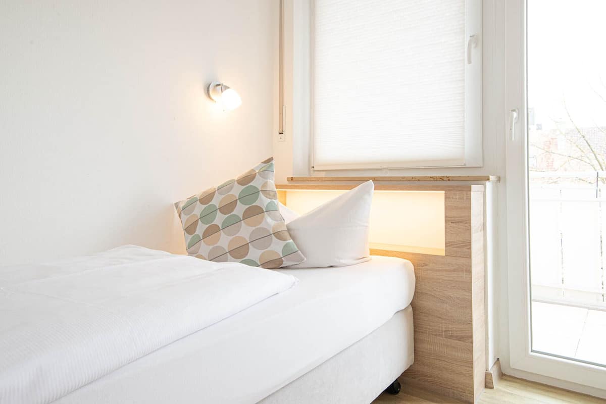 A neatly made bed with white bedding and two pillows, one with a polka dot pattern.