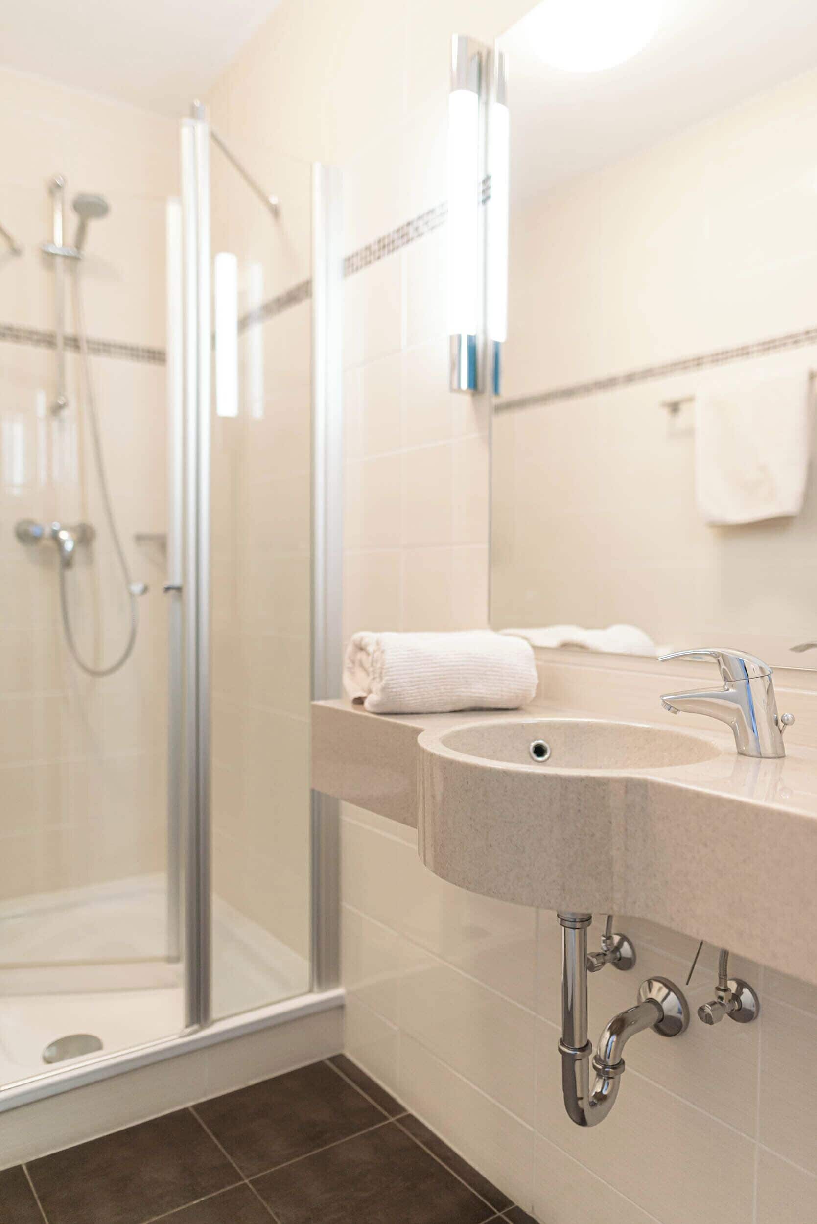 Un baño con cabina de ducha de vidrio, un lavamanos con toalla y un espejo.