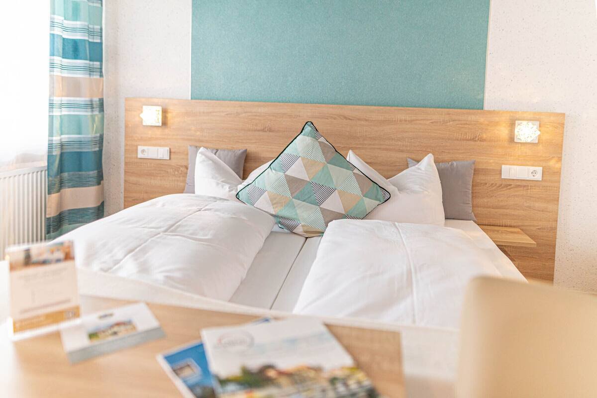 A neatly made bed with white bedding and a geometric-patterned pillow, a wooden headboard, and a light blue accent wall.