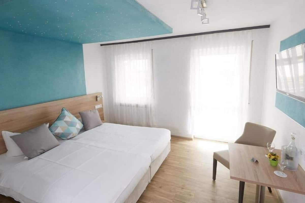 A hotel room with a large bed, a wooden headboard, a dining table with a chair, and a TV mounted on the wall.