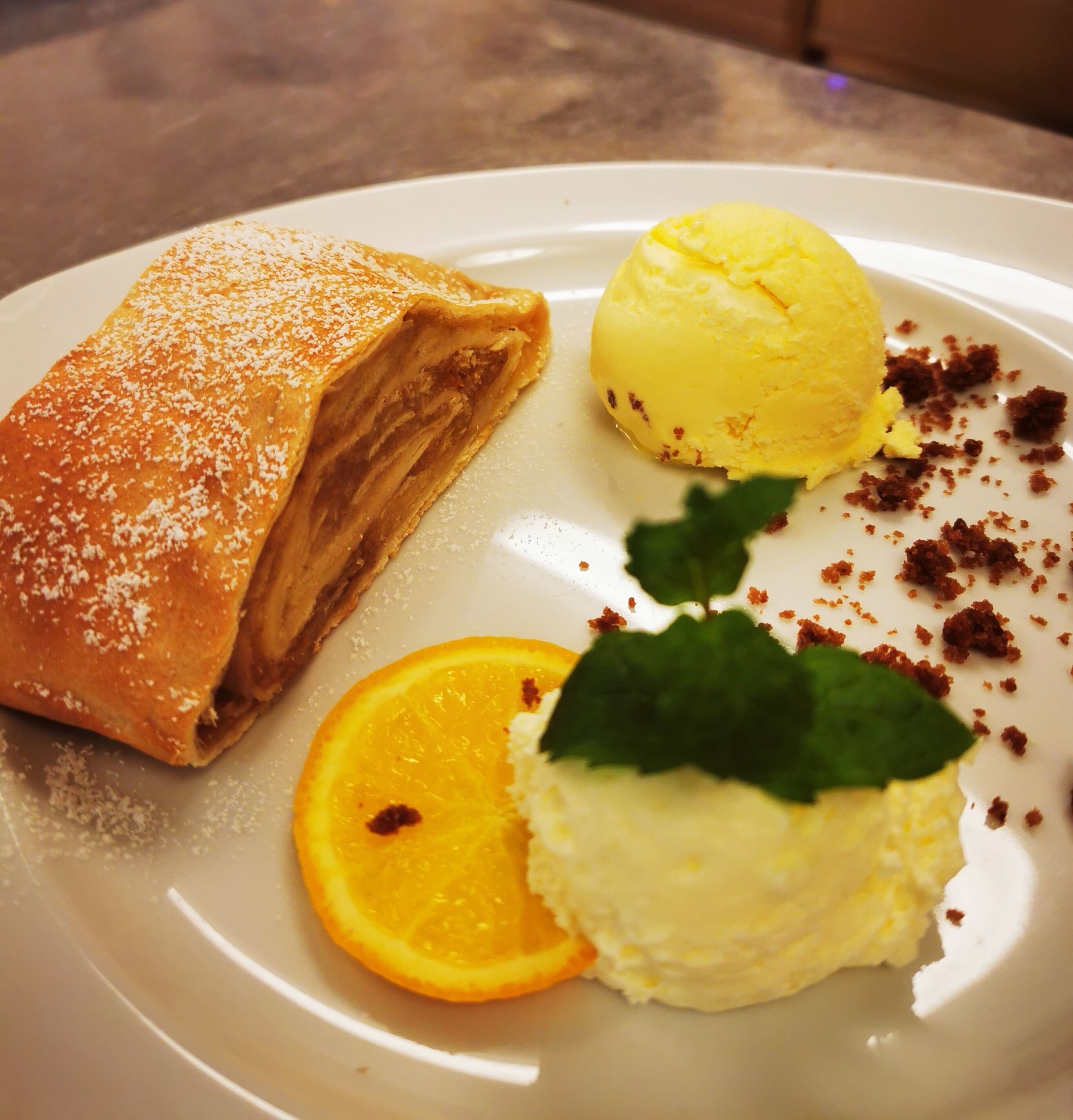 Ein Desserteller mit Gebäck, einer Kugel Eis und einer Orangenscheibe.
