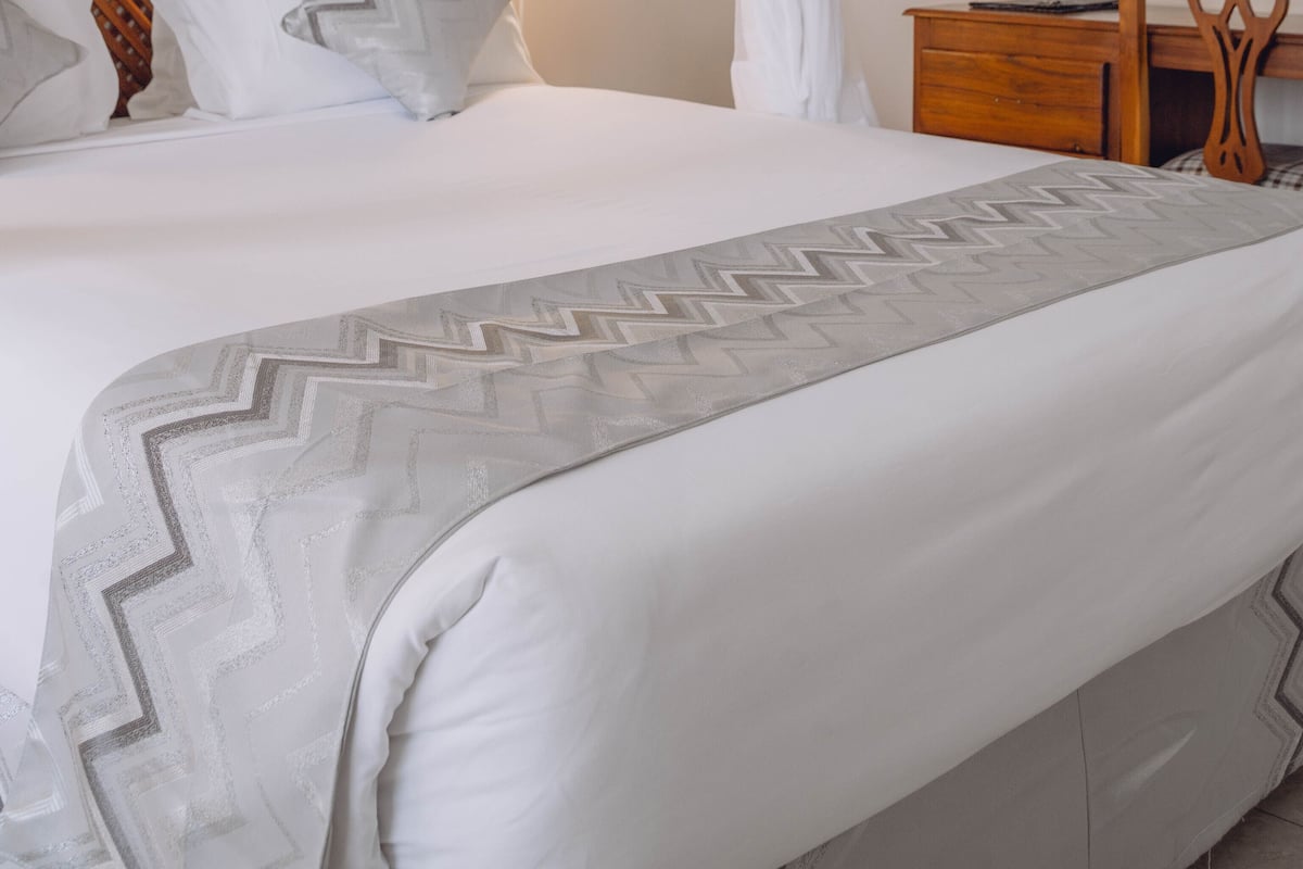 A neatly made bed with a canopy, a bedside lamp, a wooden nightstand, and a mirror.