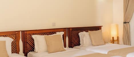 A hotel room with three beds, wooden headboards, beige bedding, and a bedside lamp.
