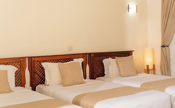 Une chambre d’hôtel avec trois lits, des têtes de lit en bois, une literie de couleur beige et une lampe de chevet.