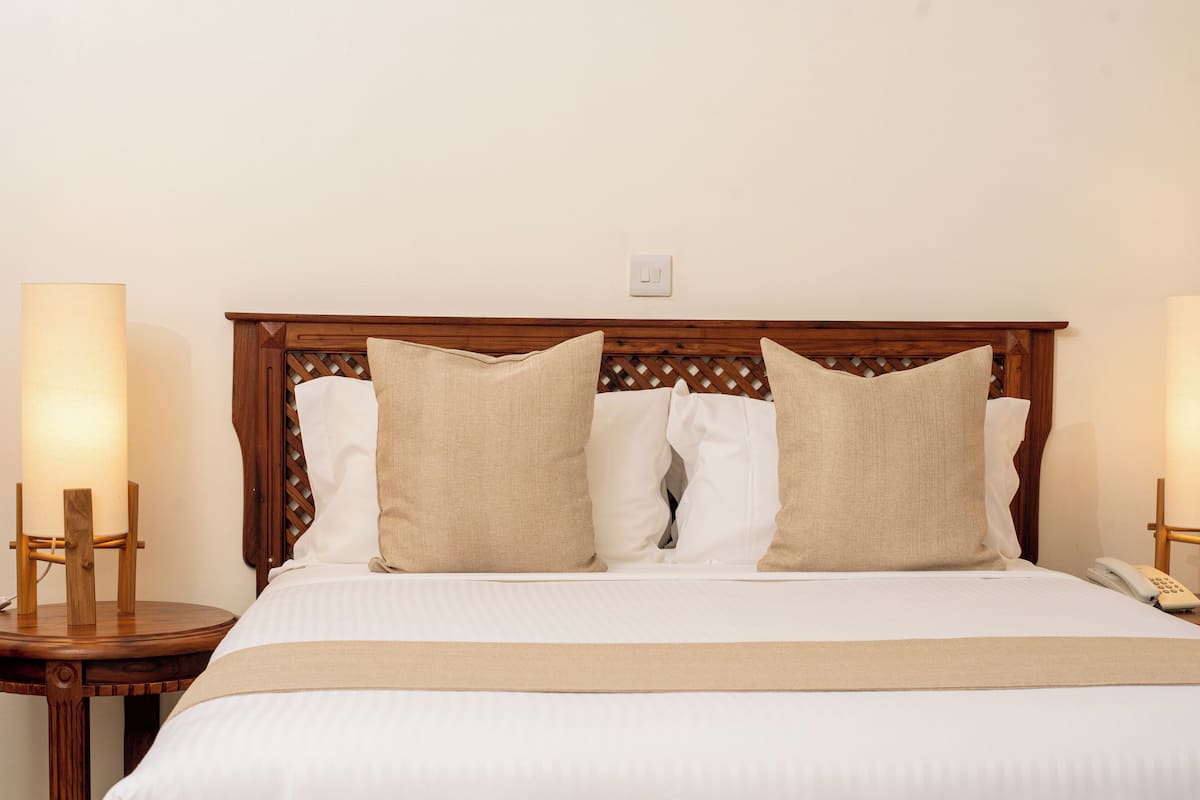A neatly made bed with a wooden headboard, two bedside lamps, and a bedside phone.