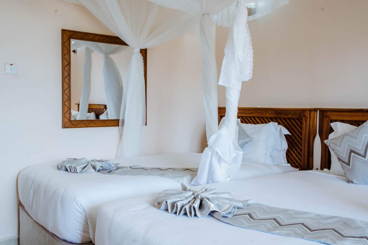 A bed with white bedding and a canopy, a wooden headboard, and a mirror on the wall.