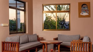 A living room with a grey sofa, wooden coffee table, and a large window with a view of greenery. - Forest Hill Hotel (Arusha)