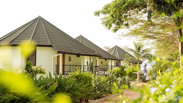 A row of bungalow-style hotel rooms with pitched roofs, a paved walkway, and lush greenery. - Forest Hill Hotel (Arusha)