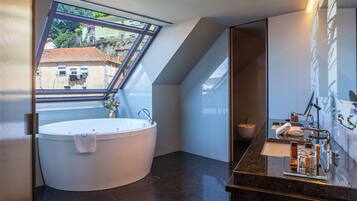 Un baño moderno con una bañera independiente, un espejo grande y vistas de la ciudad a través de un tragaluz.