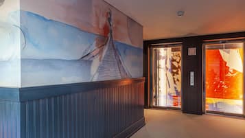 Un pasillo con un mural grande de un puente y un ascensor de vidrio decorado con arte colorido.
