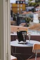 Een tafel met een zwarte emmer, waarin een fles en twee champagneglazen staan, op een balkon met uitzicht op een stadsgezicht.