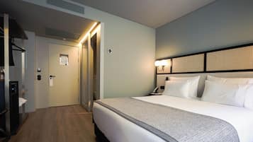 A hotel room with a bed, bedside table, lamp, and a door leading to a hallway.
