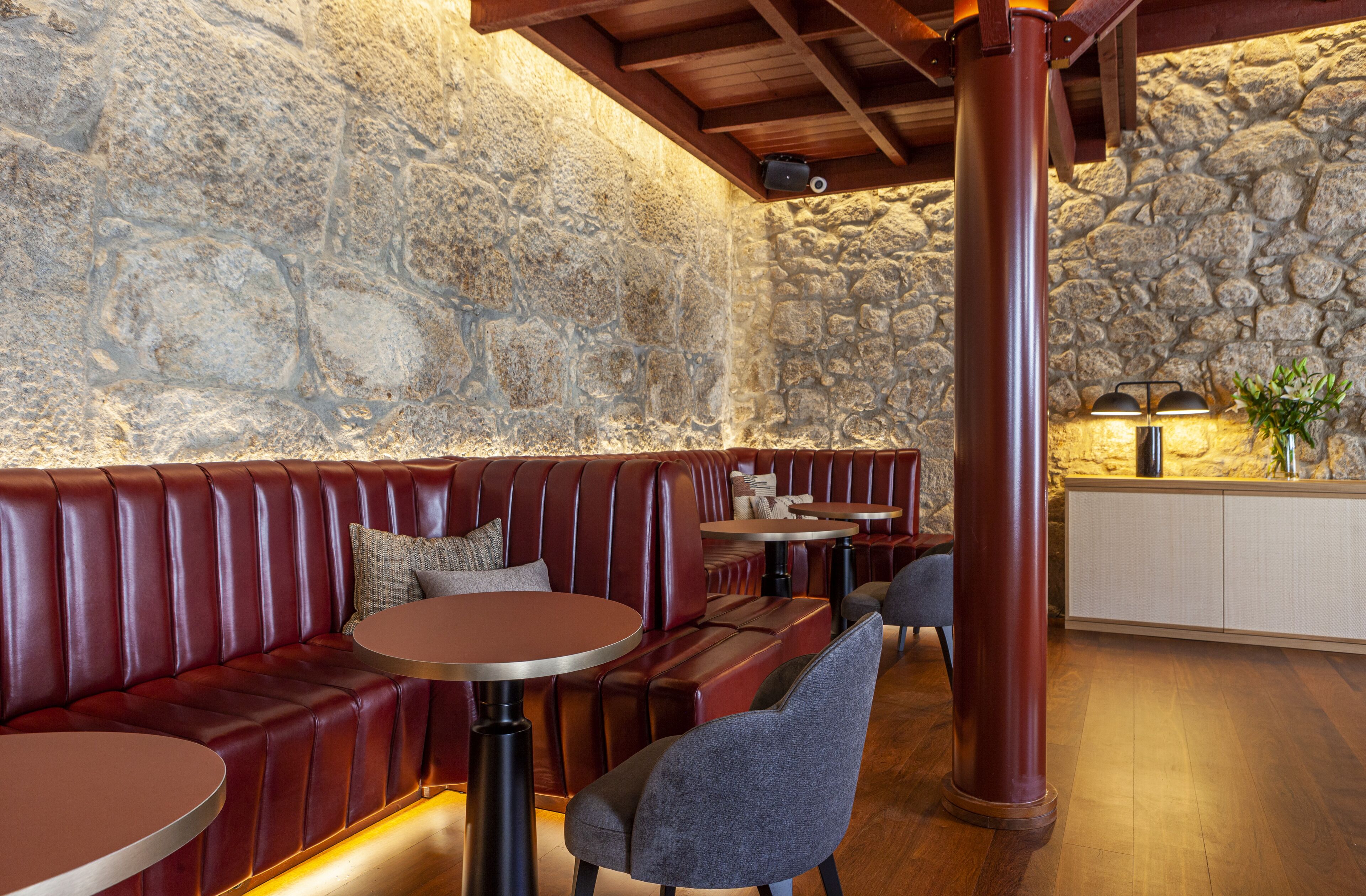 A restaurant with stone walls, leather booths, round tables, and a wooden ceiling.