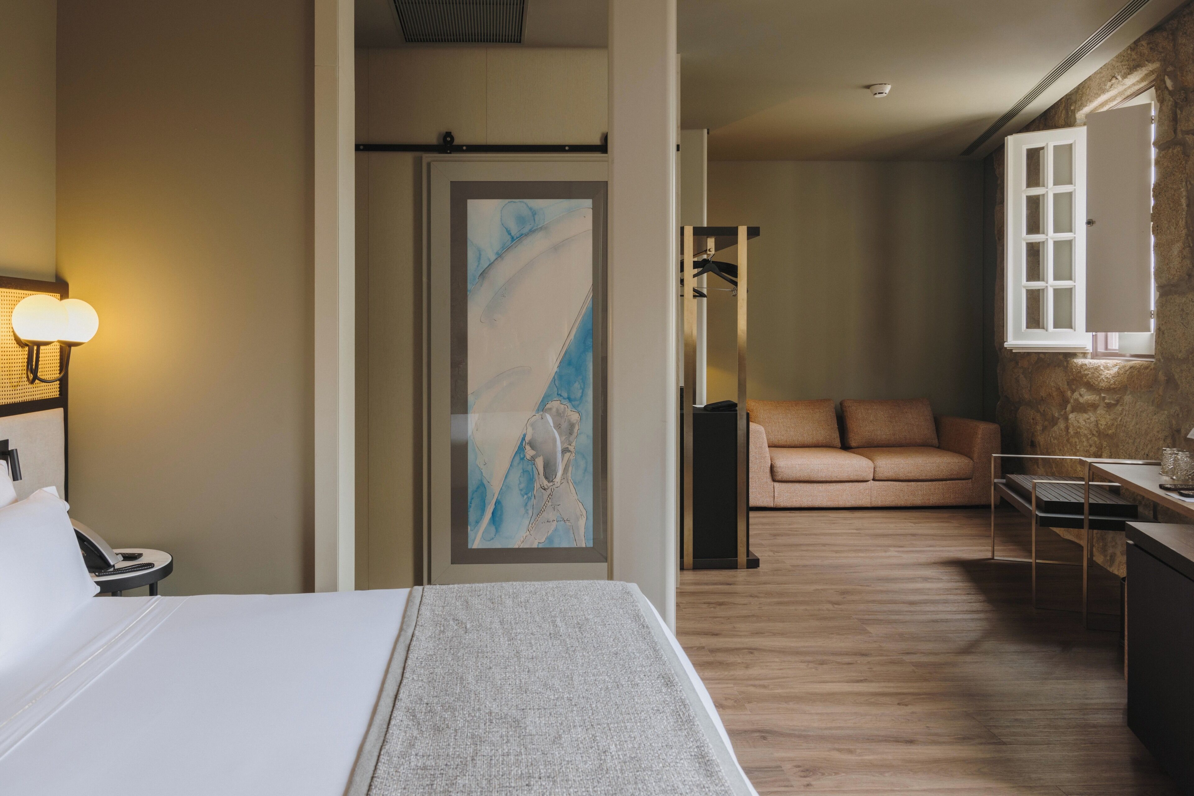 Ett hotellrum med en säng, ett skrivbord, en stol, en soffa och en tavla på väggen.