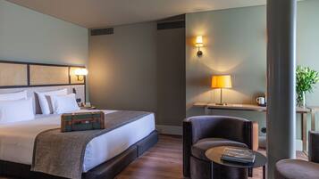 Une chambre d’hôtel avec un grand lit, une table de chevet, une lampe et un coin salon comprenant une chaise et une petite table.