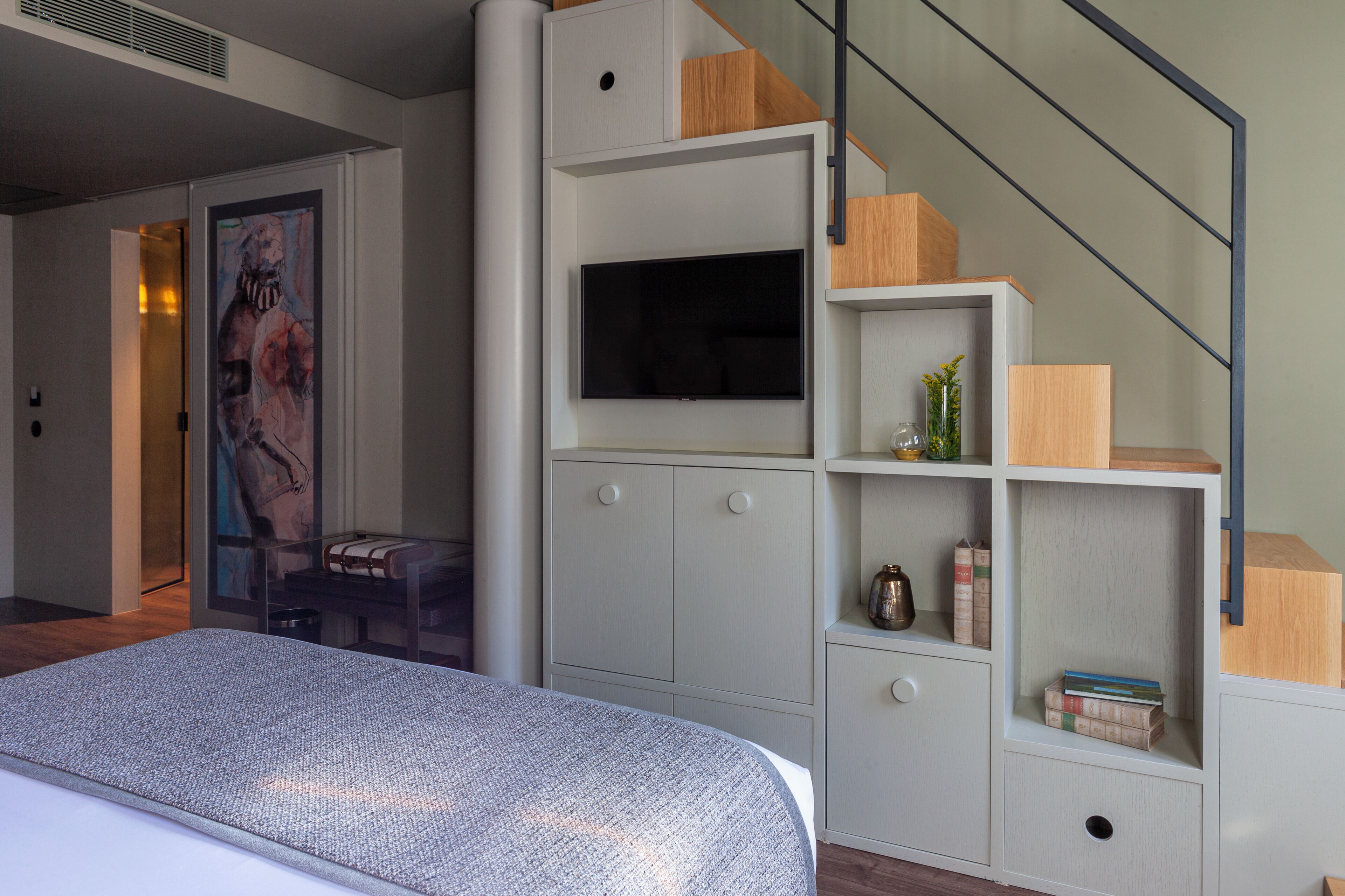A bedroom with a bed, a TV, and a built-in bookshelf with a staircase.