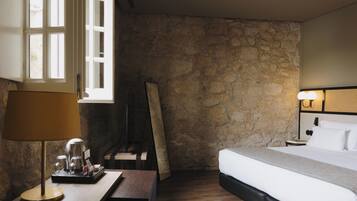 Quarto de hotel com parede de pedra, uma cama, mesa de cabeceira com abajur e uma janela.
