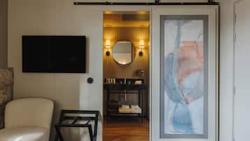 Un baño moderno con un espejo grande, un cuadro abstracto enmarcado, un lavamanos con marco negro y un perchero para toallas.