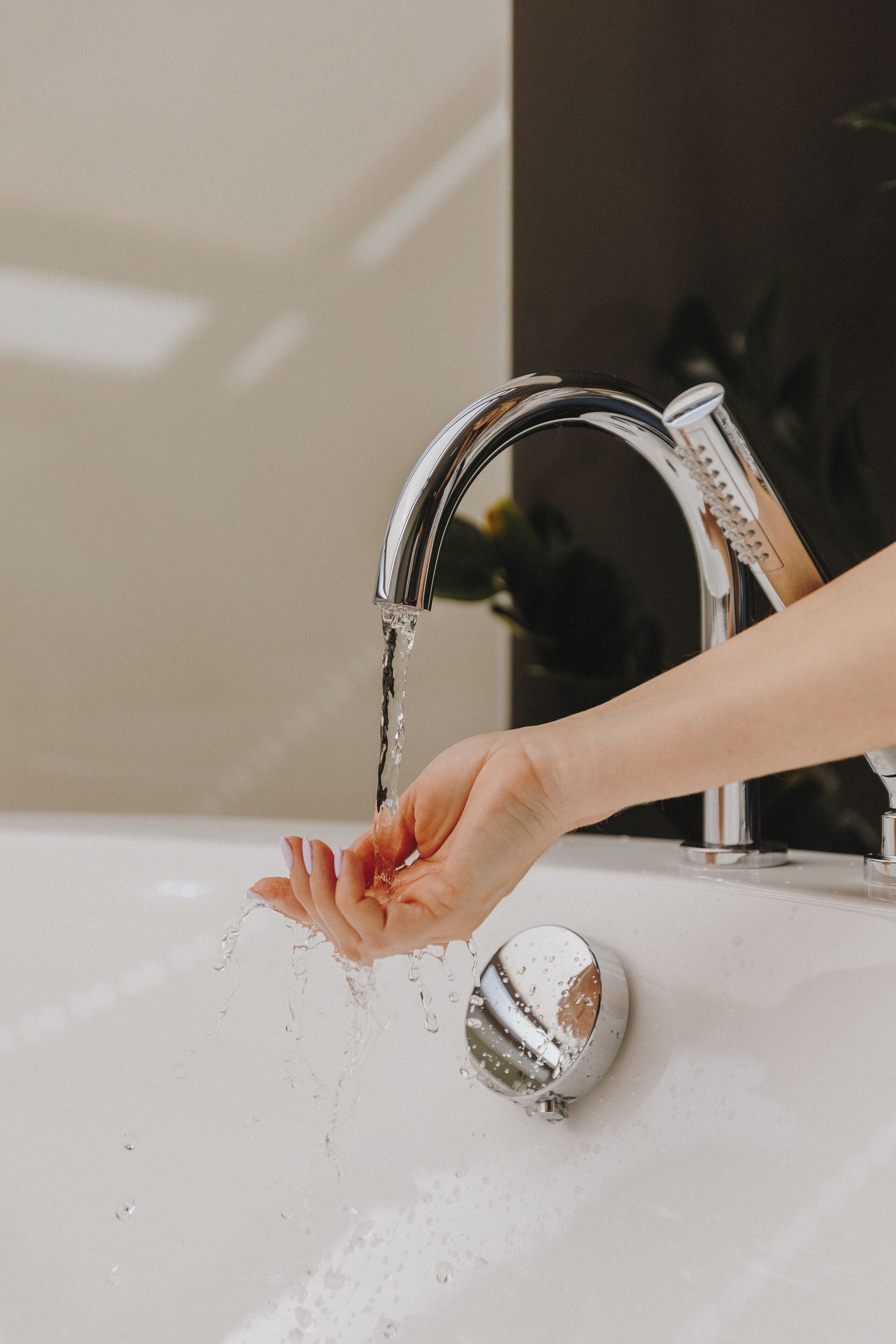 A hand under a running faucet with water splashing onto a white sink.