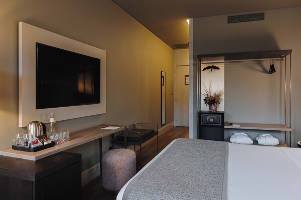 Habitación de hotel moderna con una cama grande, un escritorio con silla, un televisor de pantalla plana en la pared, un espejo y una planta pequeña.