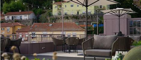 An outdoor seating area with tables and chairs, umbrellas, and a view of buildings in the background.
