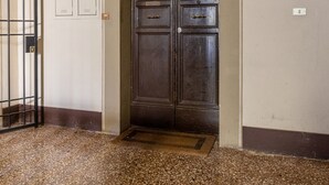 Um corredor com uma grande porta de madeira, um portão de metal e um candeeiro sobre a porta.