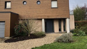 A two-story house with a flat roof, a brick chimney, and a front door with a black door frame. - Modern country house with spacious rooms and swimming pool (Doingt)