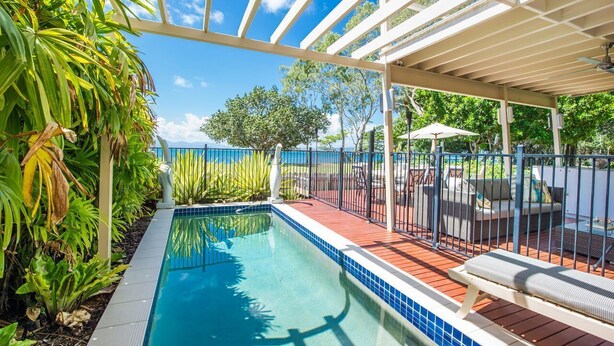 A swimming pool with a tiled edge, surrounded by plants and a covered patio area with outdoor furniture. - EEAST on Picnic (Picnic Bay)