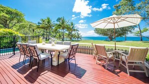 A wooden deck with a table and chairs, overlooking a scenic ocean view with palm trees. - EEAST on Picnic (Picnic Bay)