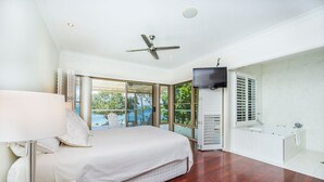 A bedroom with a bed, a TV, a window, and a bathroom. - EEAST on Picnic (Picnic Bay)