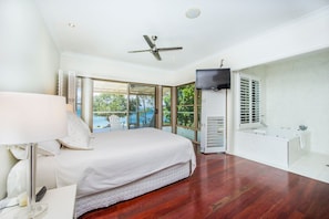 A bedroom with a bed, a TV, a window, and a bathroom. - EEAST on Picnic (Picnic Bay)