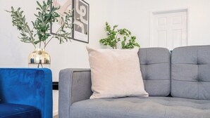 Ein graues Sofa mit einem beigen Kissen, ein blauer Sessel und zwei Blumentöpfe an einer weißen Wand.