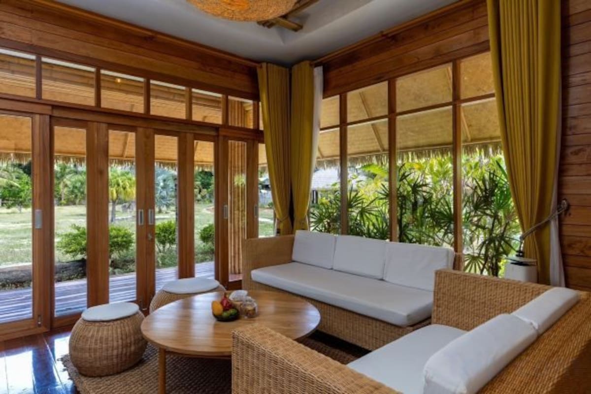 A room with a sofa, a round table, and a view of greenery outside.