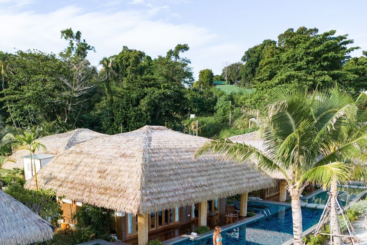 A pool area with a thatched-roof structure, a clear blue pool, and surrounding greenery.