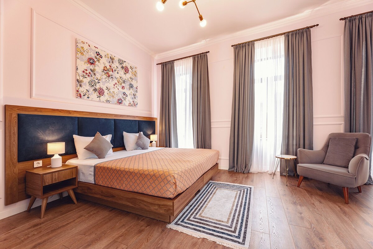 A hotel room with a large bed, a chair, a small table, and a decorative wall piece.