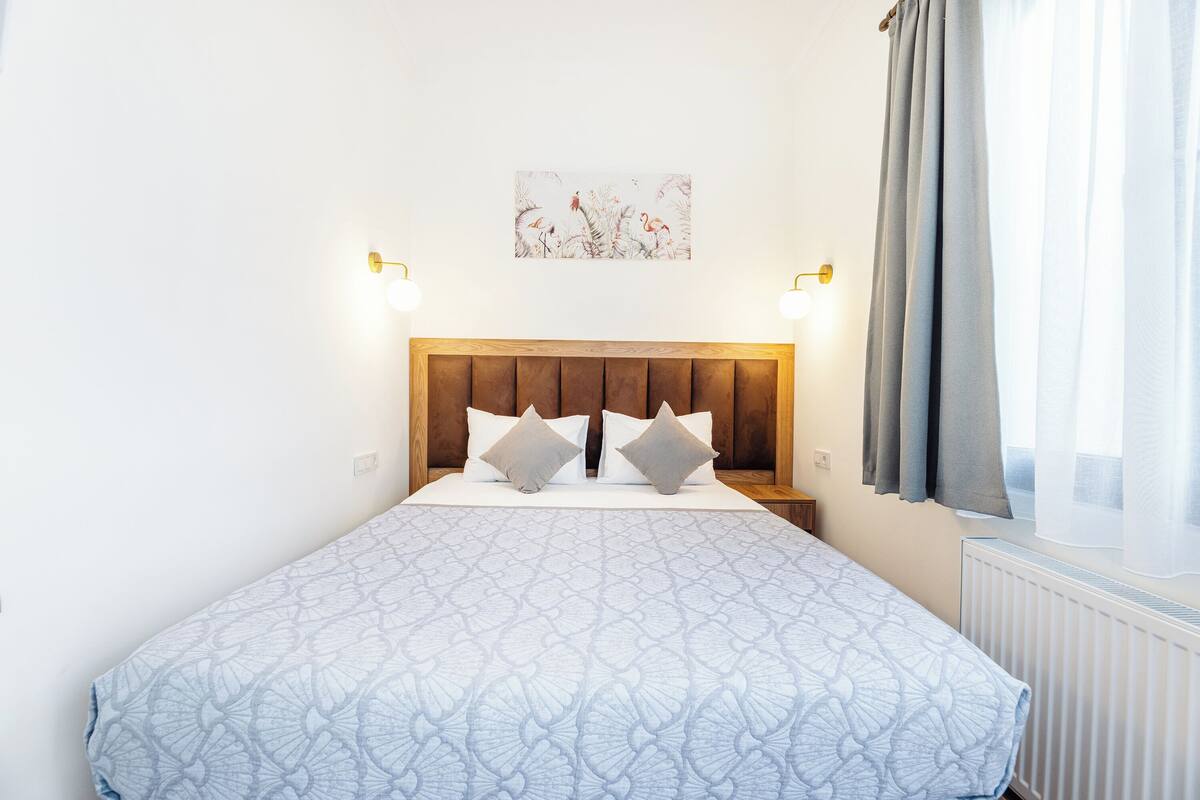 A neatly made bed with a patterned bedspread, a wooden headboard, two bedside lamps, and a wall-mounted artwork.