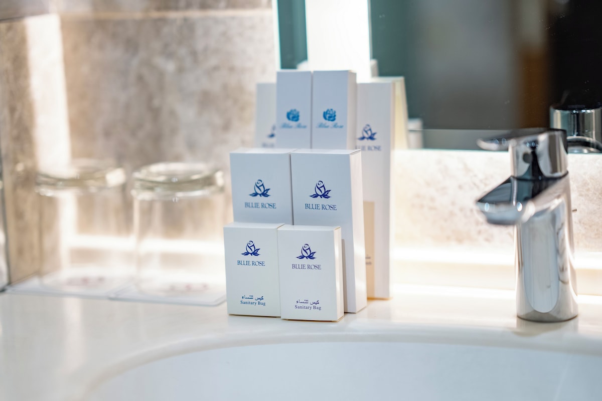 A bathroom with a sink, a mirror, and several sanitary bags labeled "Blue Rose" on the countertop.