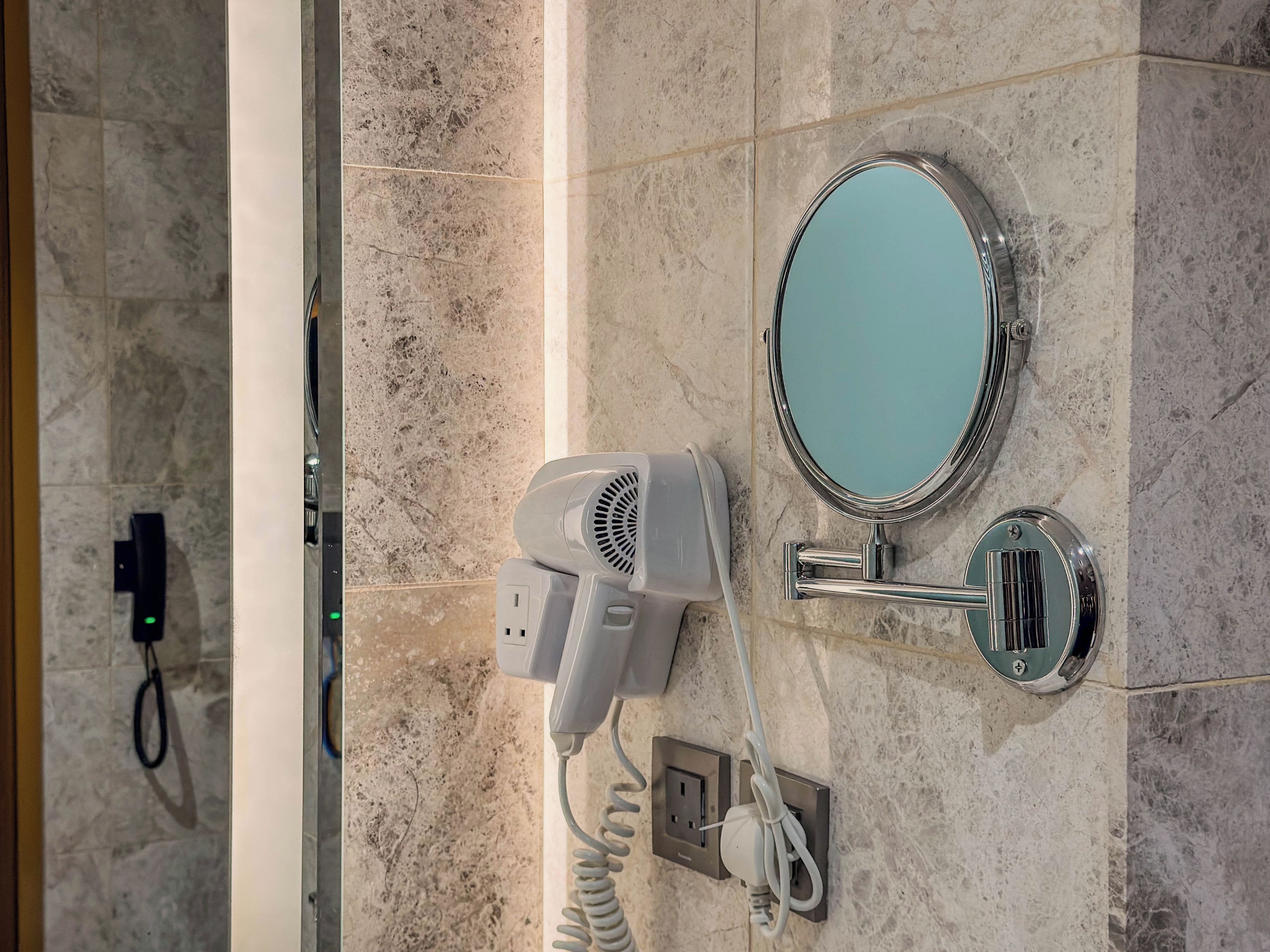 A bathroom with a hairdryer, a mirror, and a wall-mounted light switch.