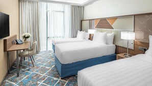 Quarto de hotel com duas camas, uma escrivaninha com telefone, uma cadeira, uma televisão e uma janela grande com cortinas.