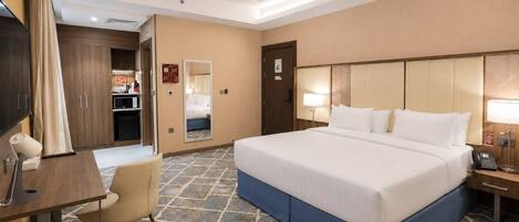 Une chambre d’hôtel avec un grand lit, un bureau avec une chaise, un miroir et une table de chevet avec une lampe.