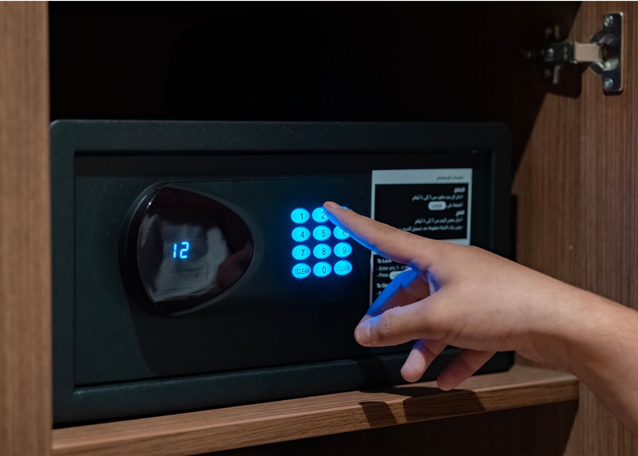 A hand pressing a button on a digital lock with a display showing the number 12.